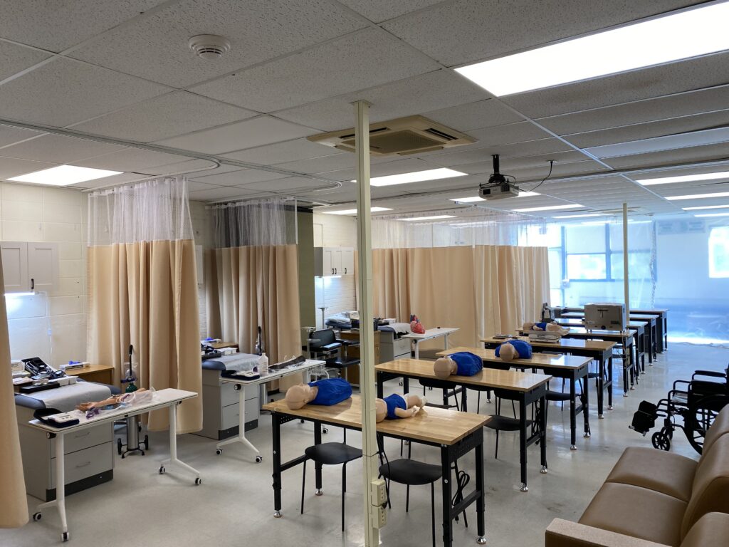 A classroom set up to look like a hospital with beds, curtains and tables with training items.